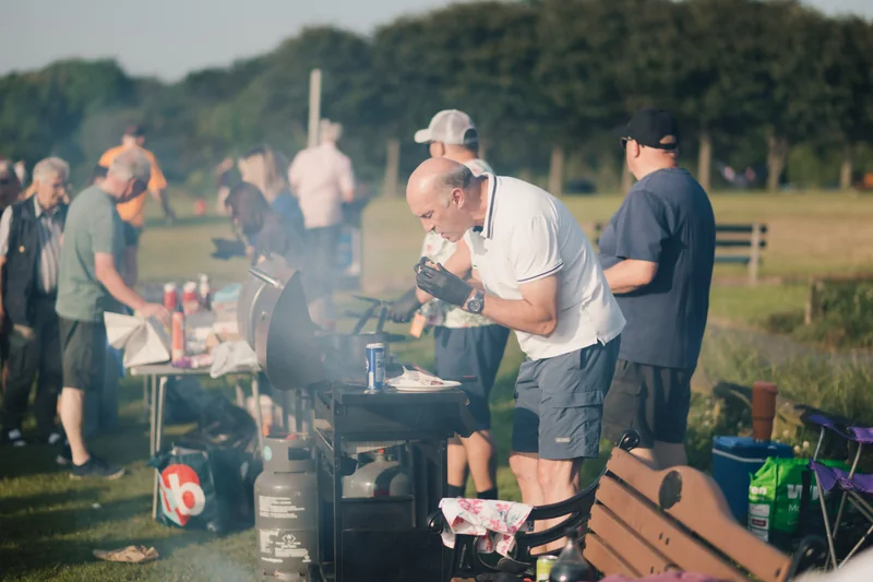 a group of people standing around a barbecue grill in a park