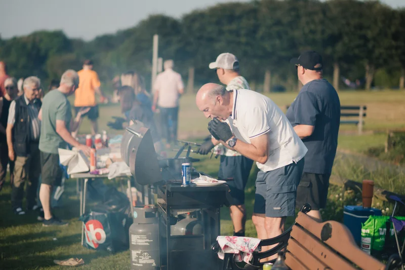 a group of people grilling on a barbecue in a park