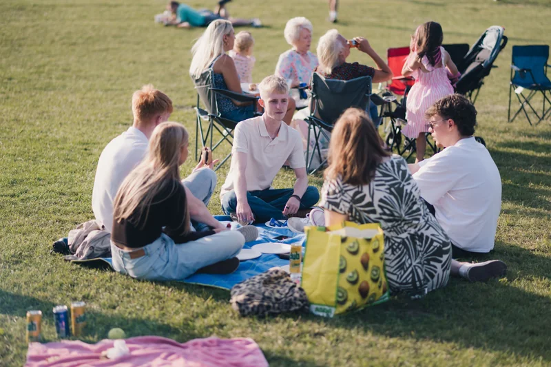 a group of people sitting on a blanket in a grassy field
