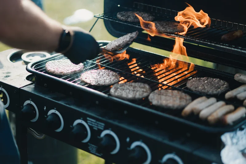 a man grilling burgers and hotdogs on a barbecue grill