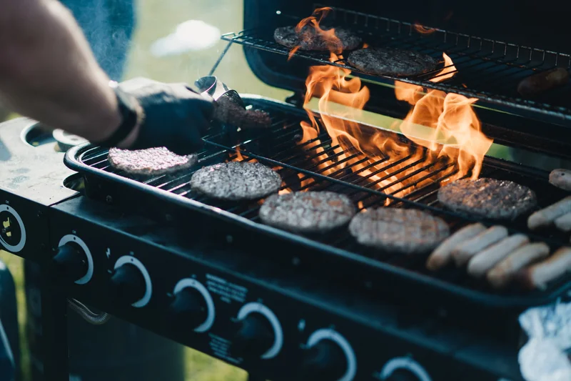 a man grilling burgers and hotdogs on a barbecue grill