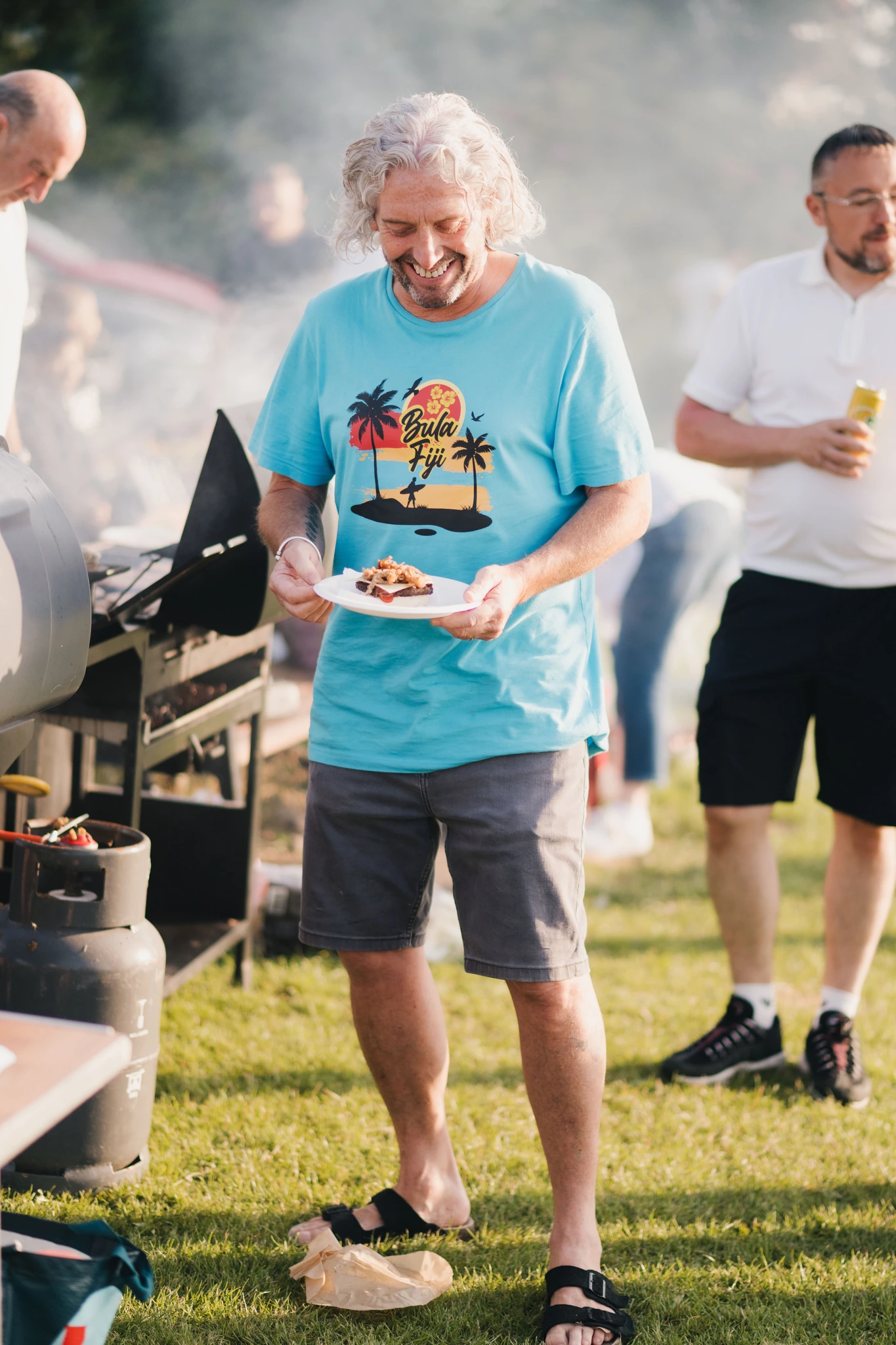 a man with a plate of food in front of a barbeque grill