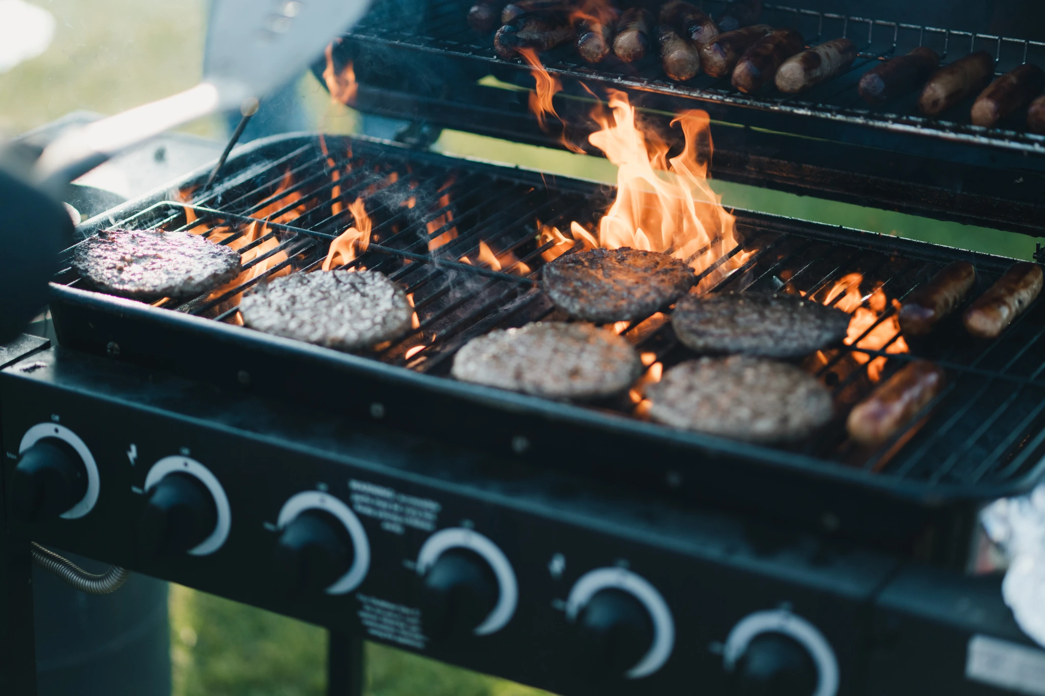 a person grilling burgers and hotdogs on a grill