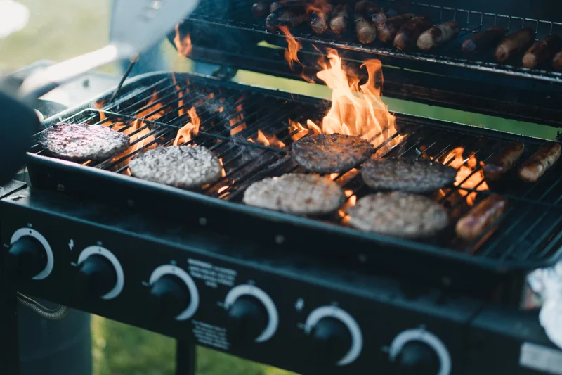 a person grilling burgers and hotdogs on a grill