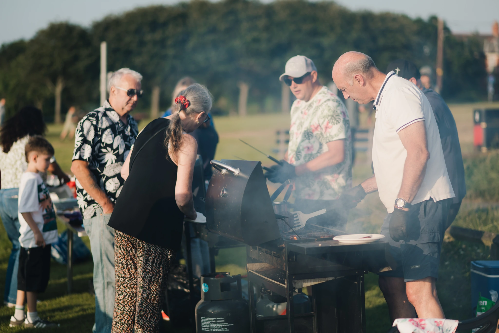 a group of people standing around a barbecue grill on a grassy field