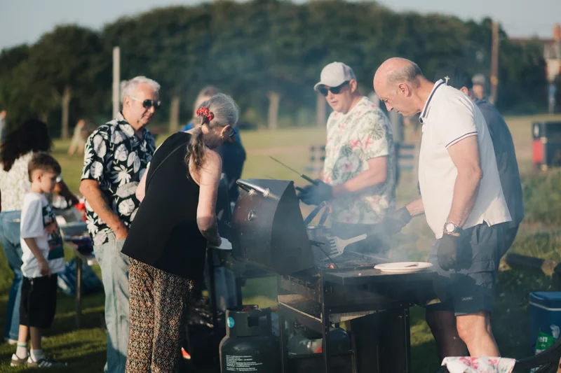 a group of people standing around a barbecue grill on a grassy field