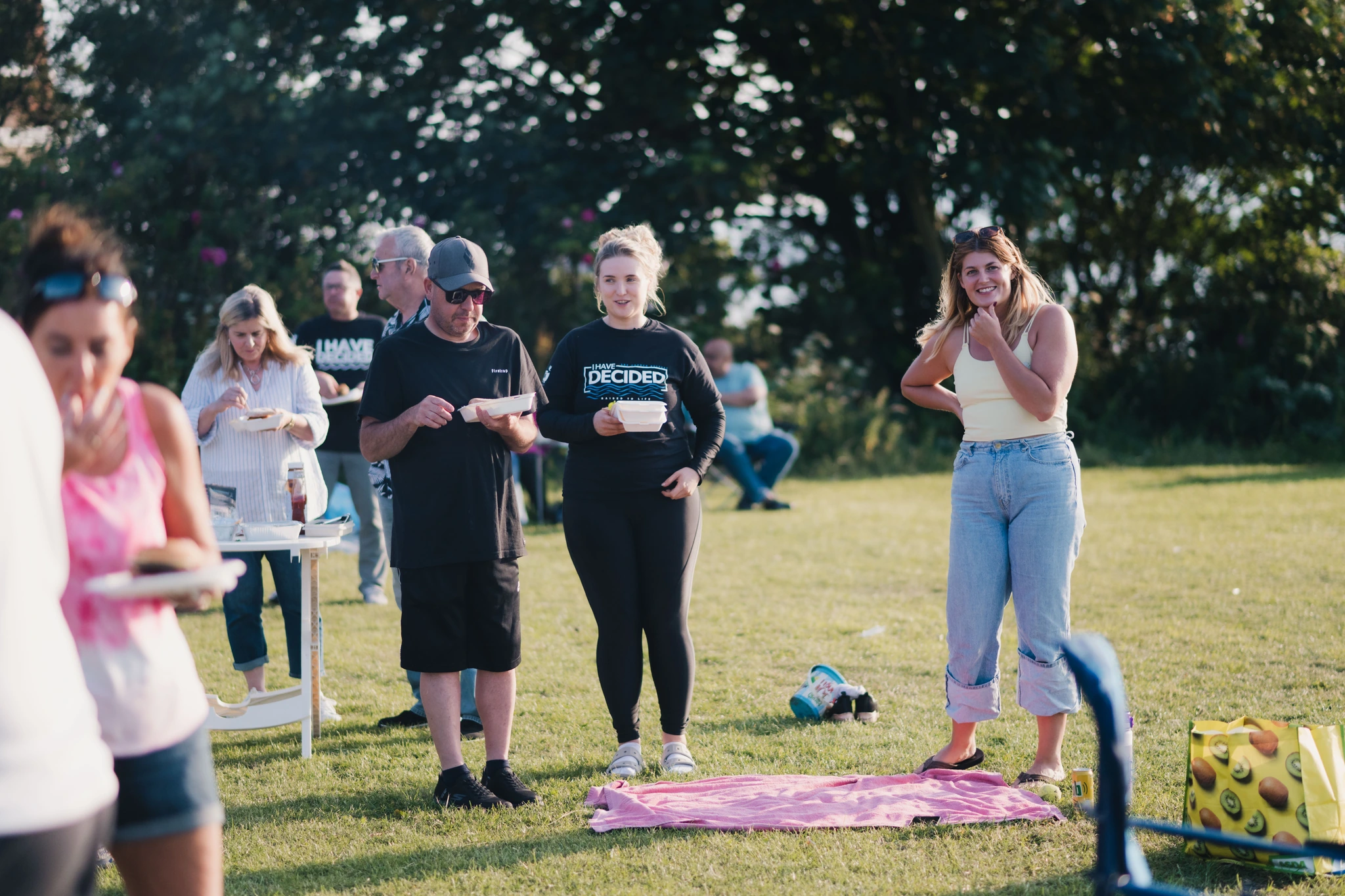 a group of people standing in a grassy area with a table and chairs