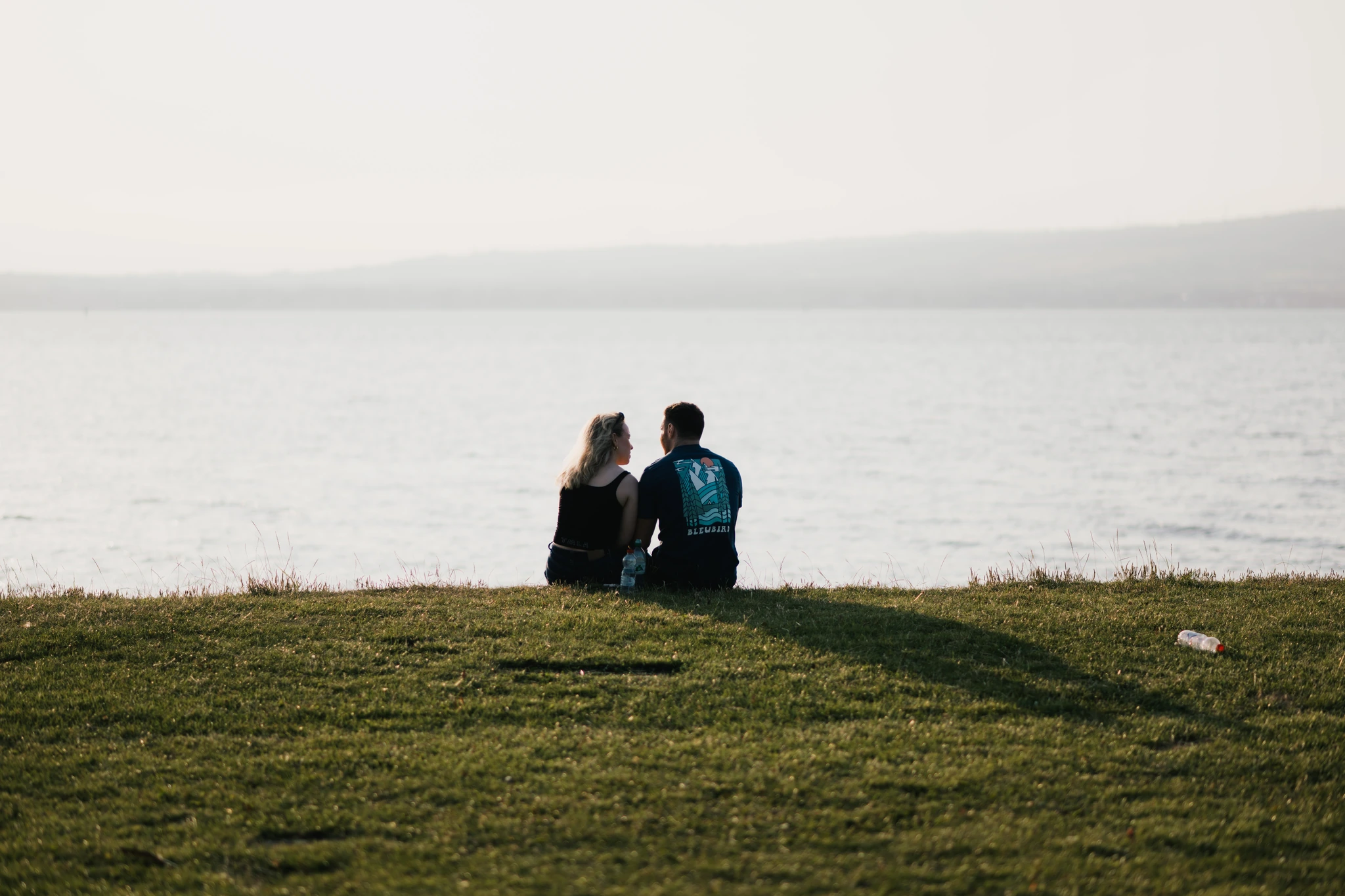 a couple sits on a grassy hill overlooking a body of water