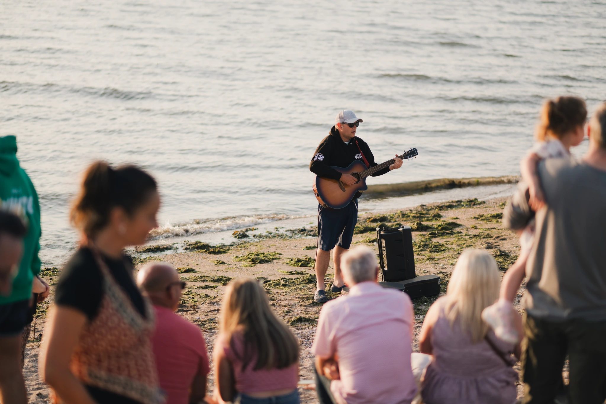 a man playing guitar on the beach in front of a crowd of people