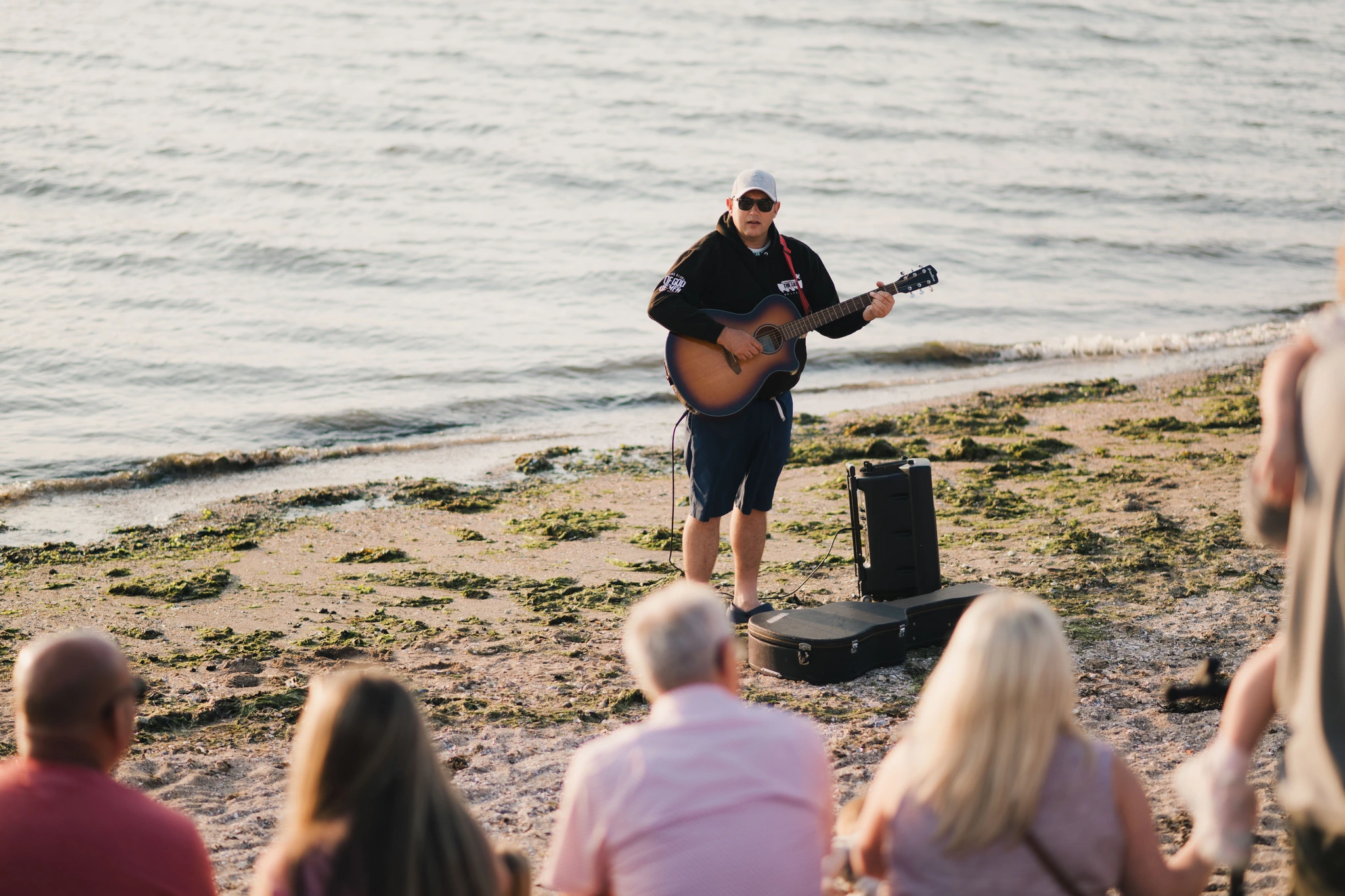 a man playing an acoustic guitar on a beach in front of a crowd