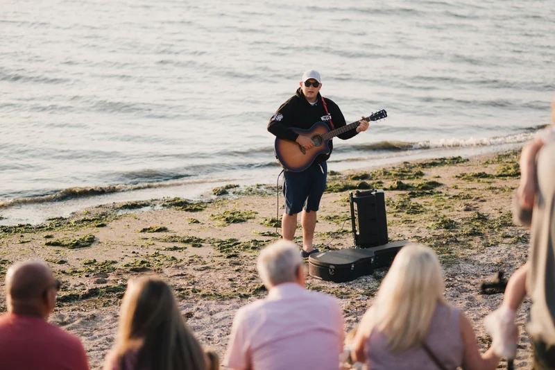 a man playing an acoustic guitar on a beach in front of a crowd