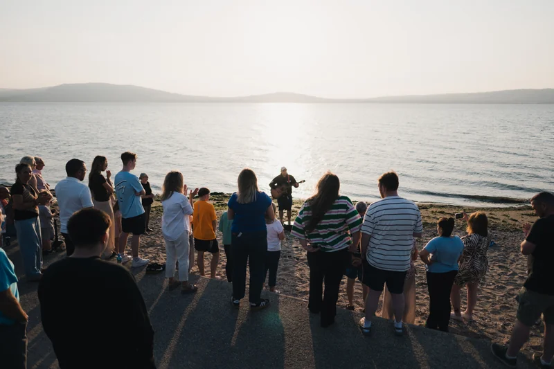 a group of people watching a sunset over a lake
