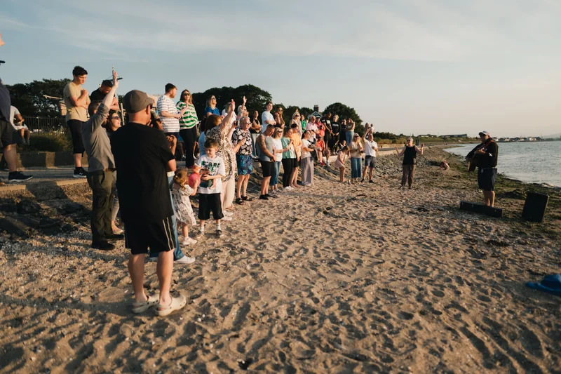a group of people standing on a beach watching the sun rise over the sea