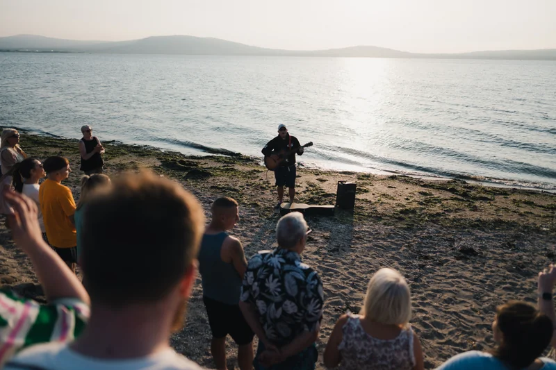 a man playing guitar on a beach in front of a crowd of people