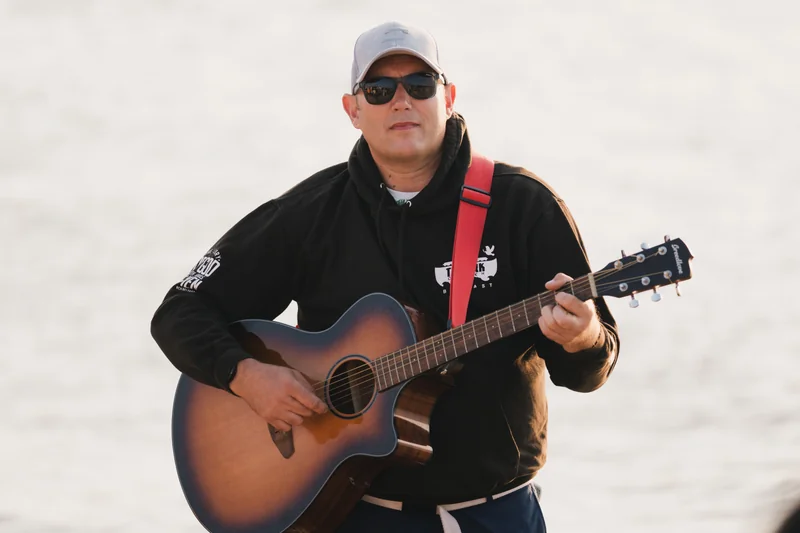 a man in sunglasses plays an acoustic guitar