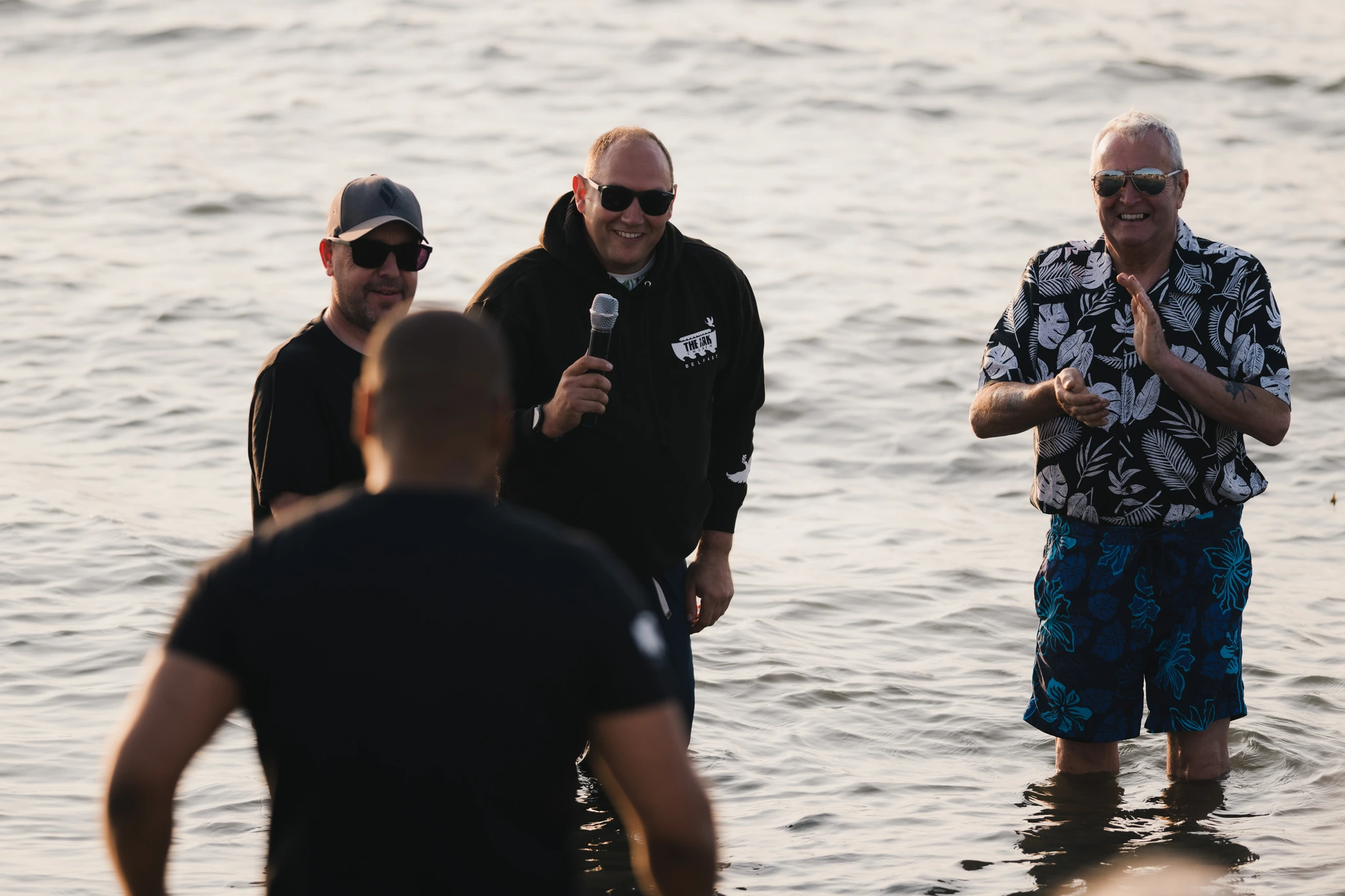 three men standing in the water with a microphone in their hands