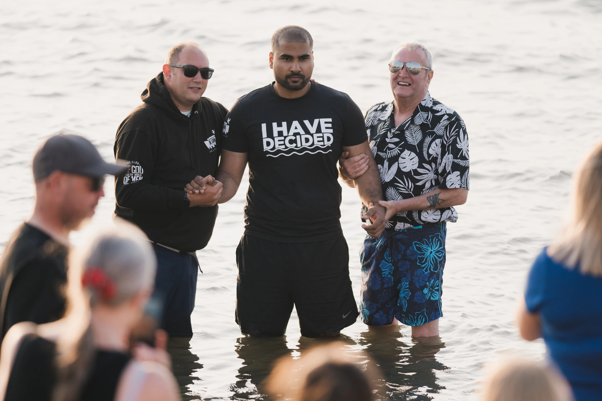 a group of men and women are standing in the water with their hands in the air