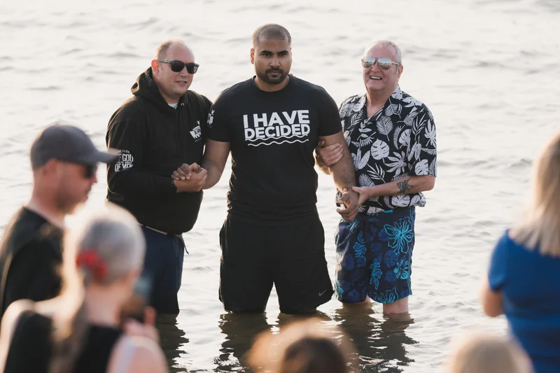 a group of men and women are standing in the water with their hands in the air