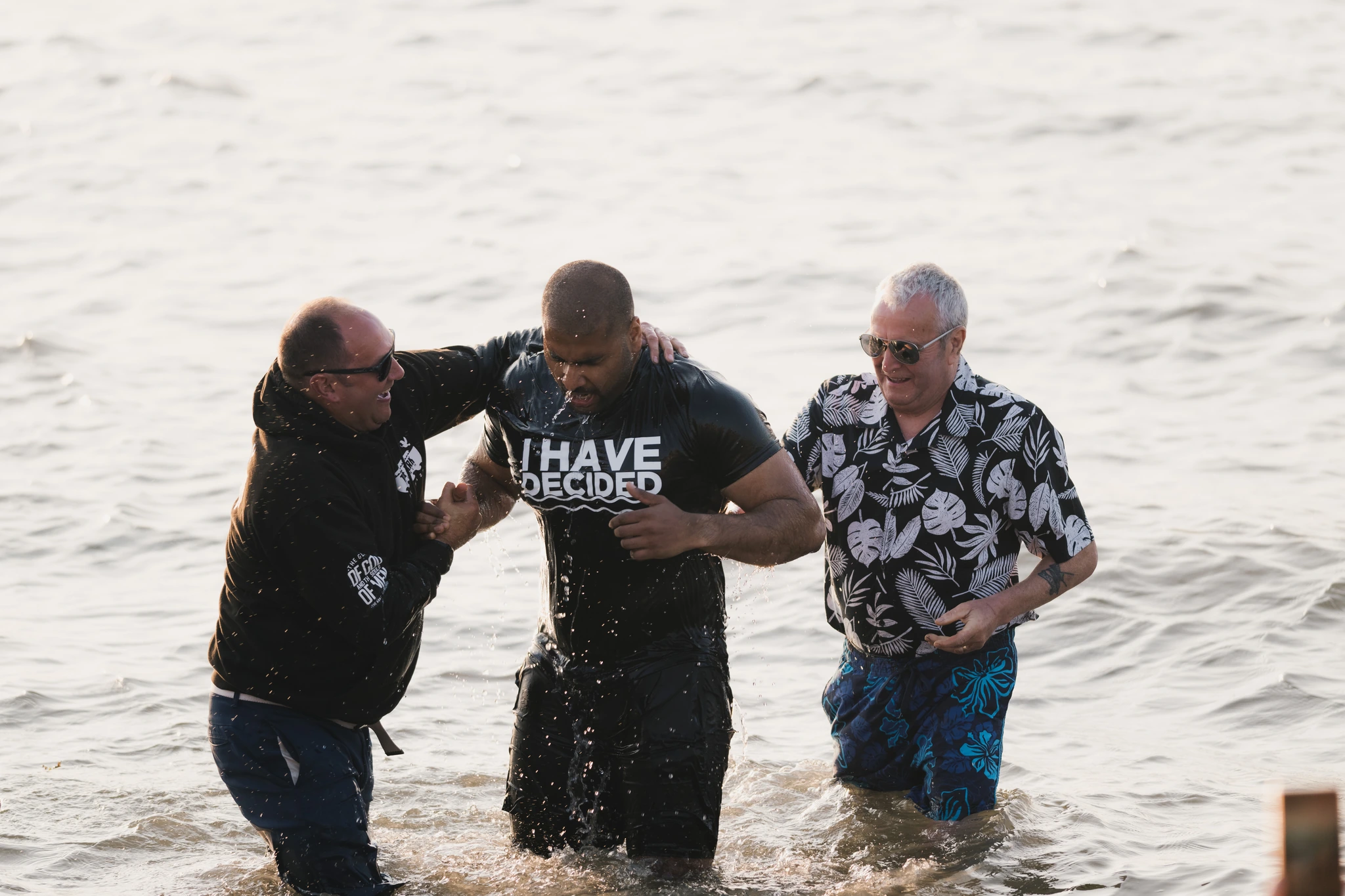 a group of men and women stand in the water at a baptism ceremony at the sacrament of the christian church in philadelphia, california