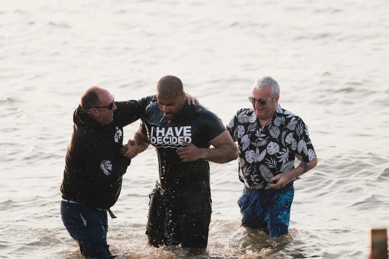 a group of men and women stand in the water at a baptism ceremony at the sacrament of the christian church in philadelphia, california
