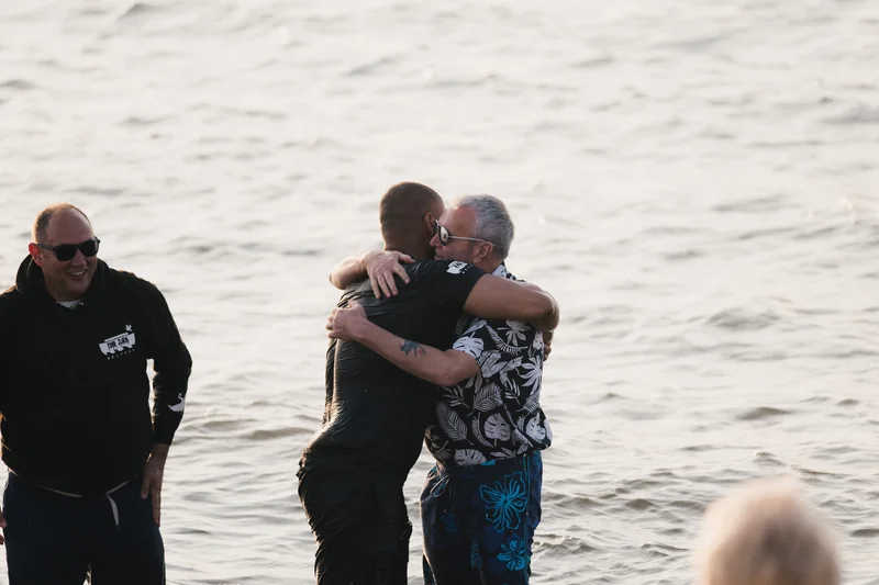 a man in a bathing suit hugs another man as he stands in the water
