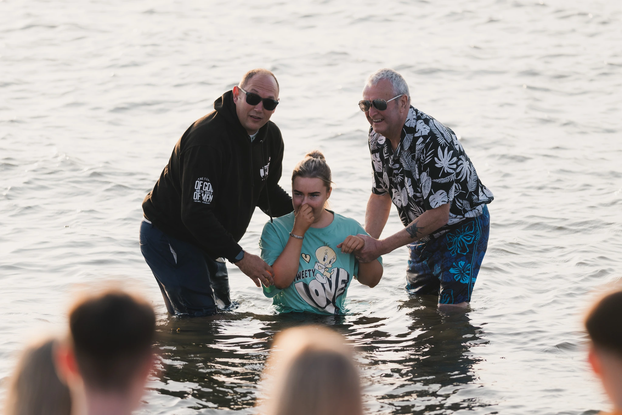 a man and woman are standing in the water while a woman holds a baby in her arms