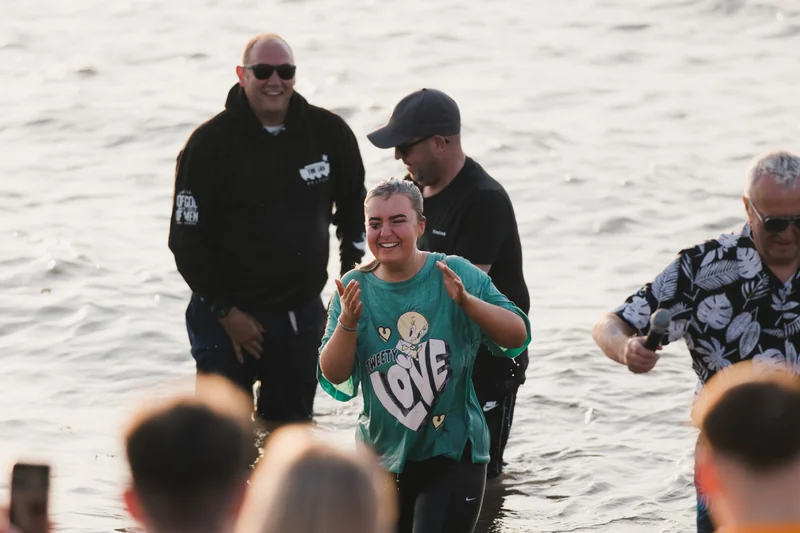 a woman walks into the water with a man in the background