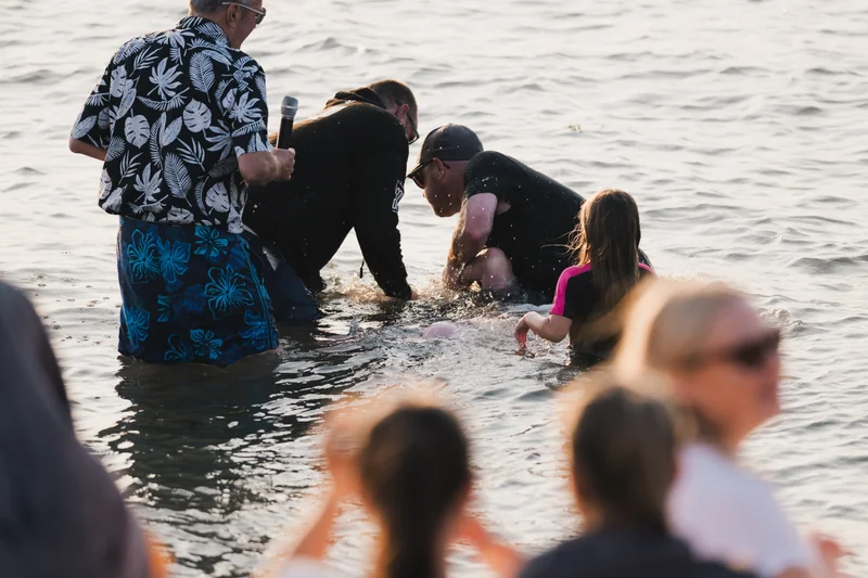 a group of people standing in the water with a baby in their lap