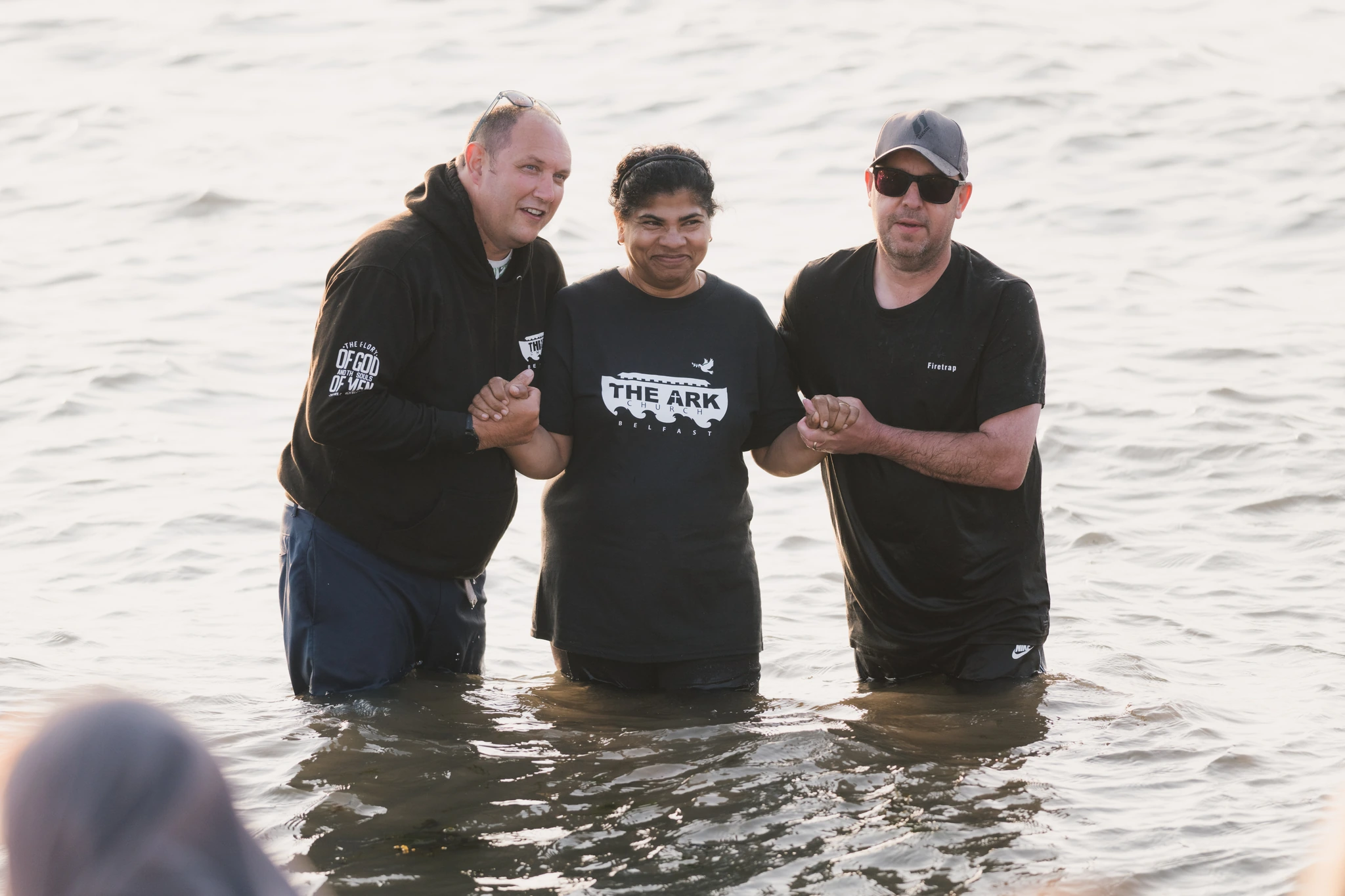 three men are standing in a body of water with their hands in the air