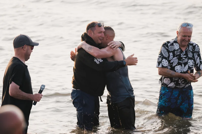 a man hugs another man in the water as he stands in front of a group of people