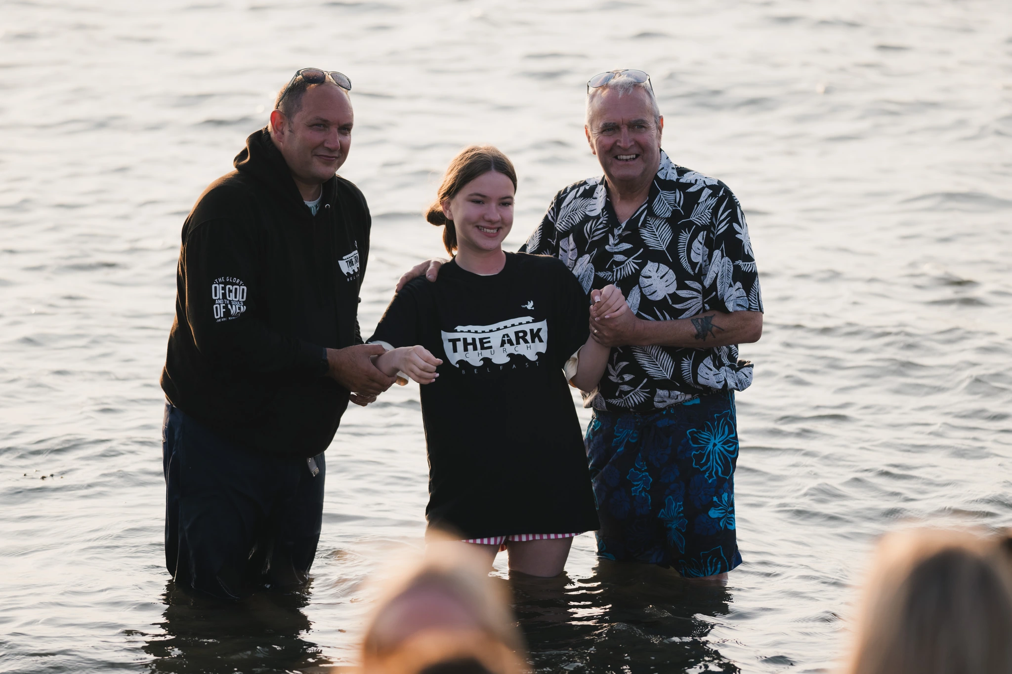 a man and woman standing in the water with a child in the background