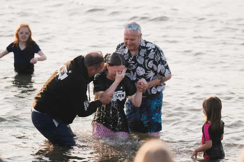 a group of people standing in the water with a baby in their lap