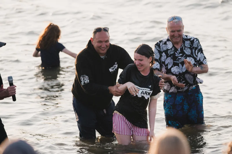 a group of people standing in the water with a woman holding a baby in her arms
