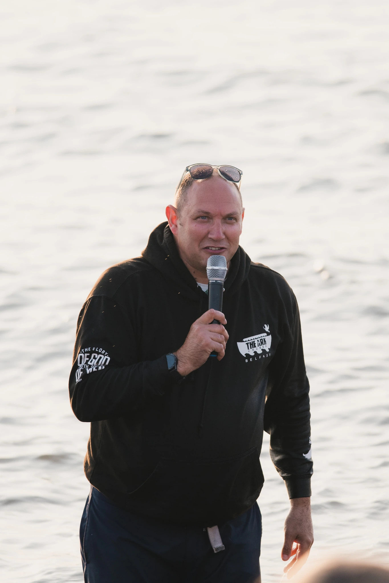 a man holding a microphone while standing in front of a body of water