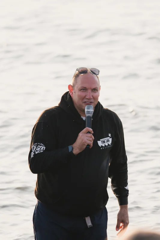 a man holding a microphone while standing in front of a body of water