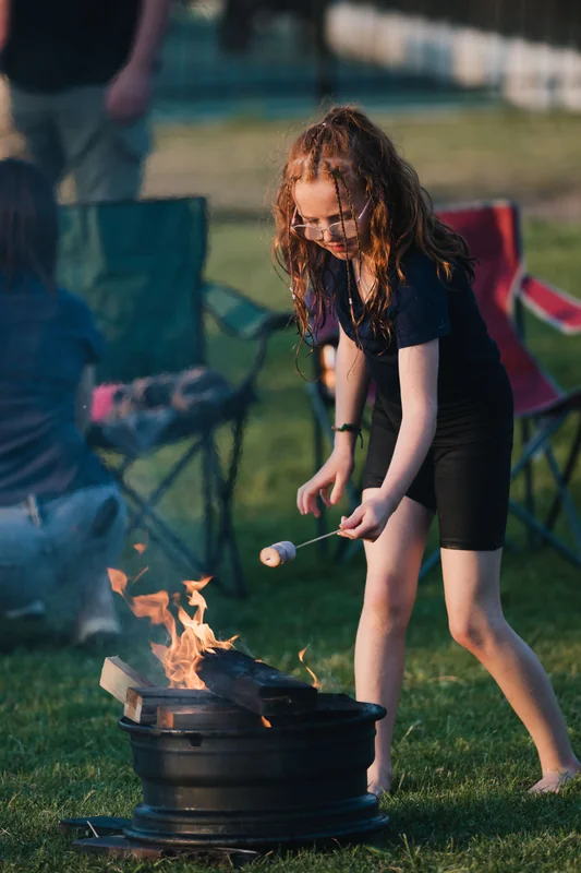 a little girl cooking on a campfire in a grassy field