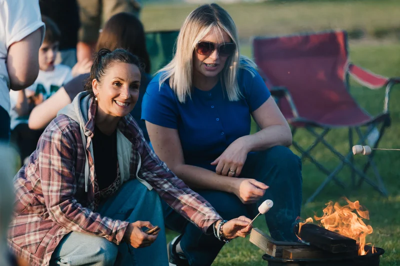 a group of people sitting around a campfire in a grassy area