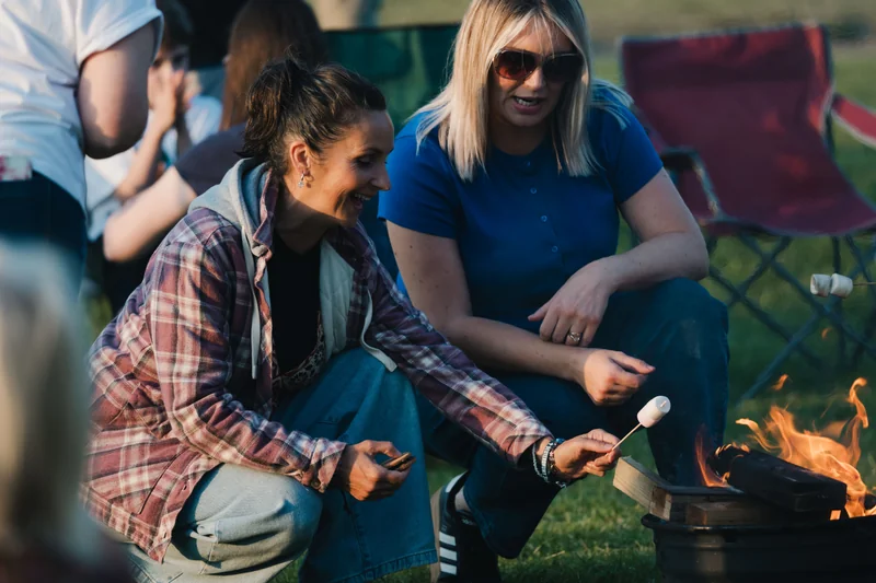 a group of women sitting around a campfire in a grassy field