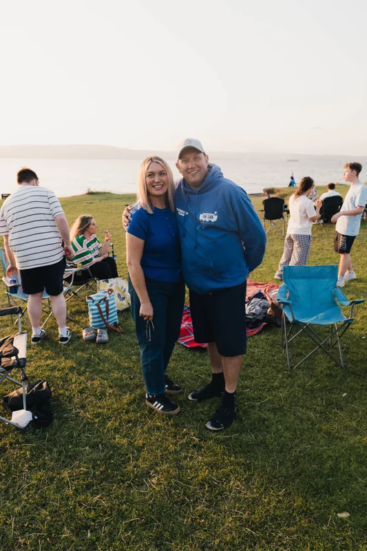 a man and woman standing in a grassy field at sunset