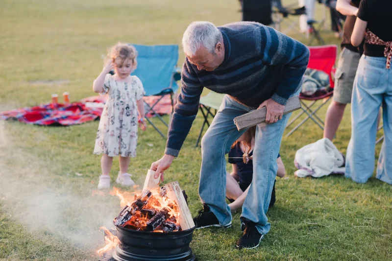 a man lighting a fire pit in the middle of a grassy field