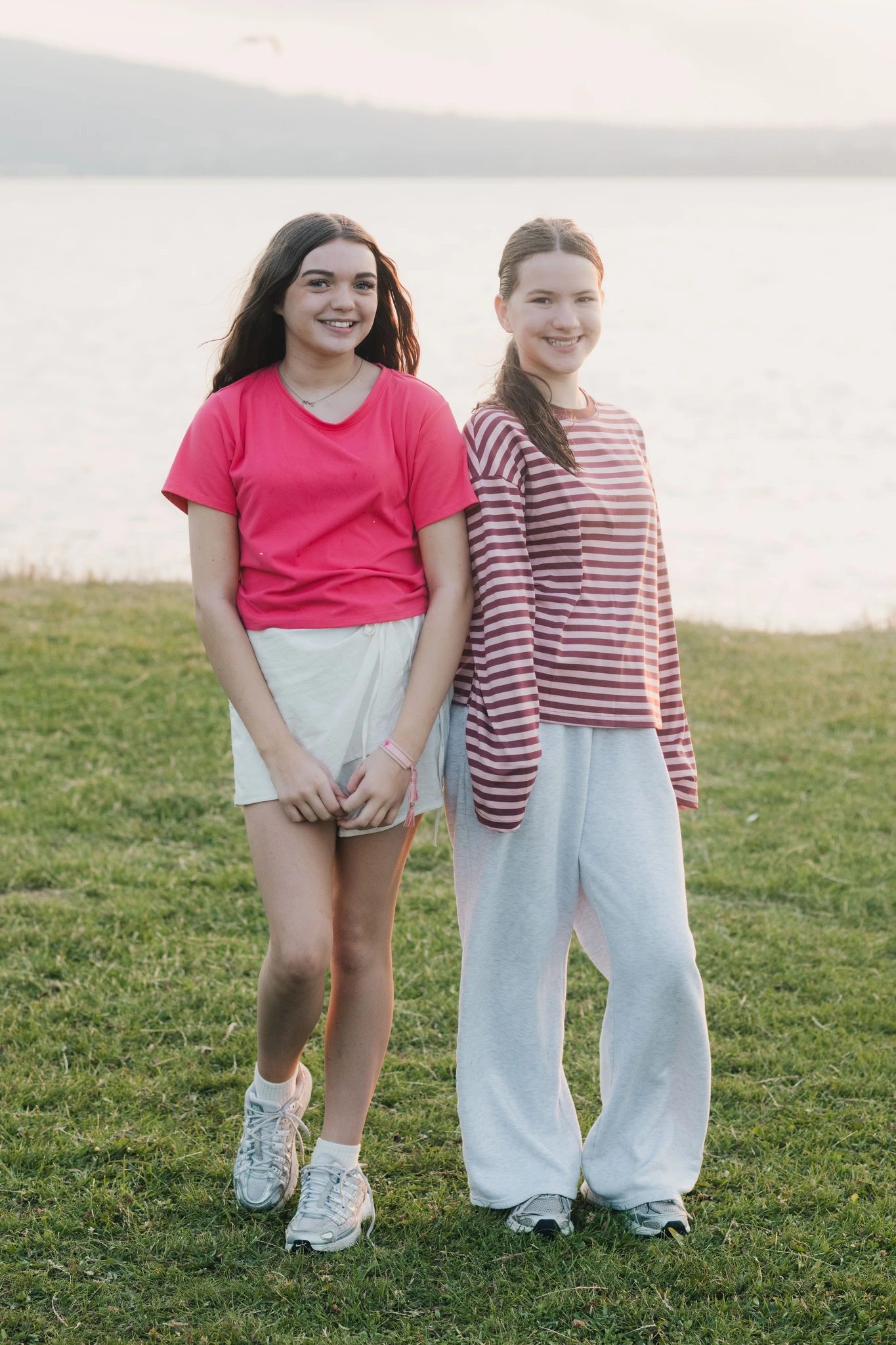 two girls standing on a grassy field with a lake in the background