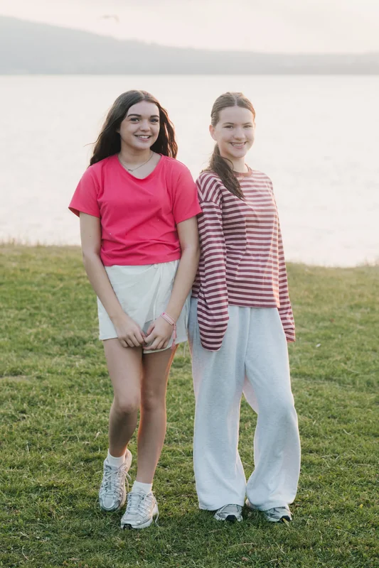 two girls standing on a grassy field with a lake in the background