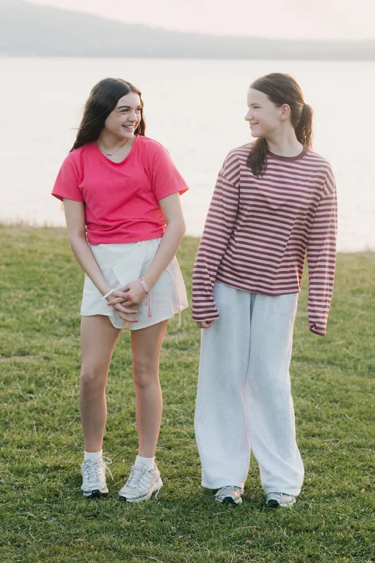 two girls standing in a grassy field with a lake in the background