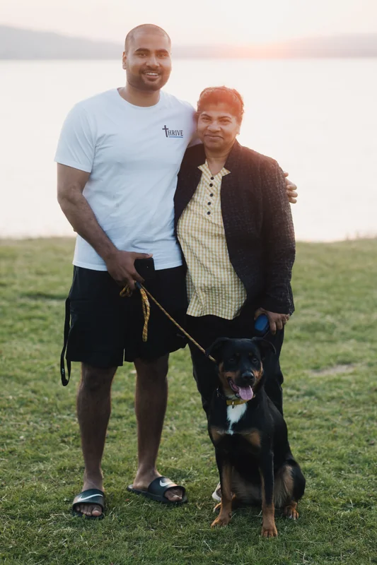 a man and woman standing in front of a lake with a dog on a leash