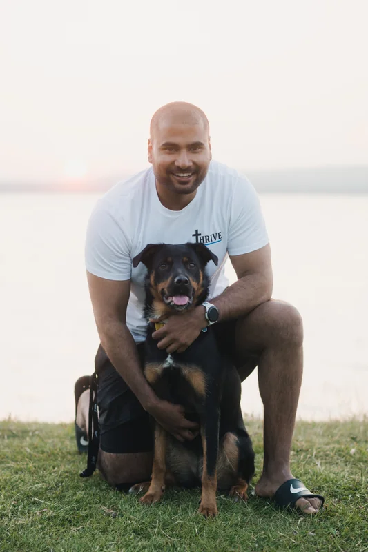 a man with a dog sitting on the grass in front of a lake
