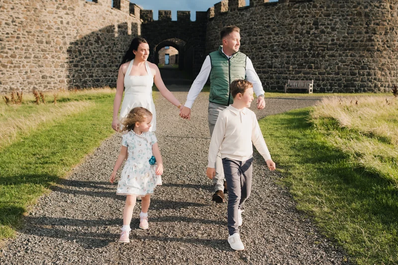 a couple and their children are walking down a stone path in front of a castle