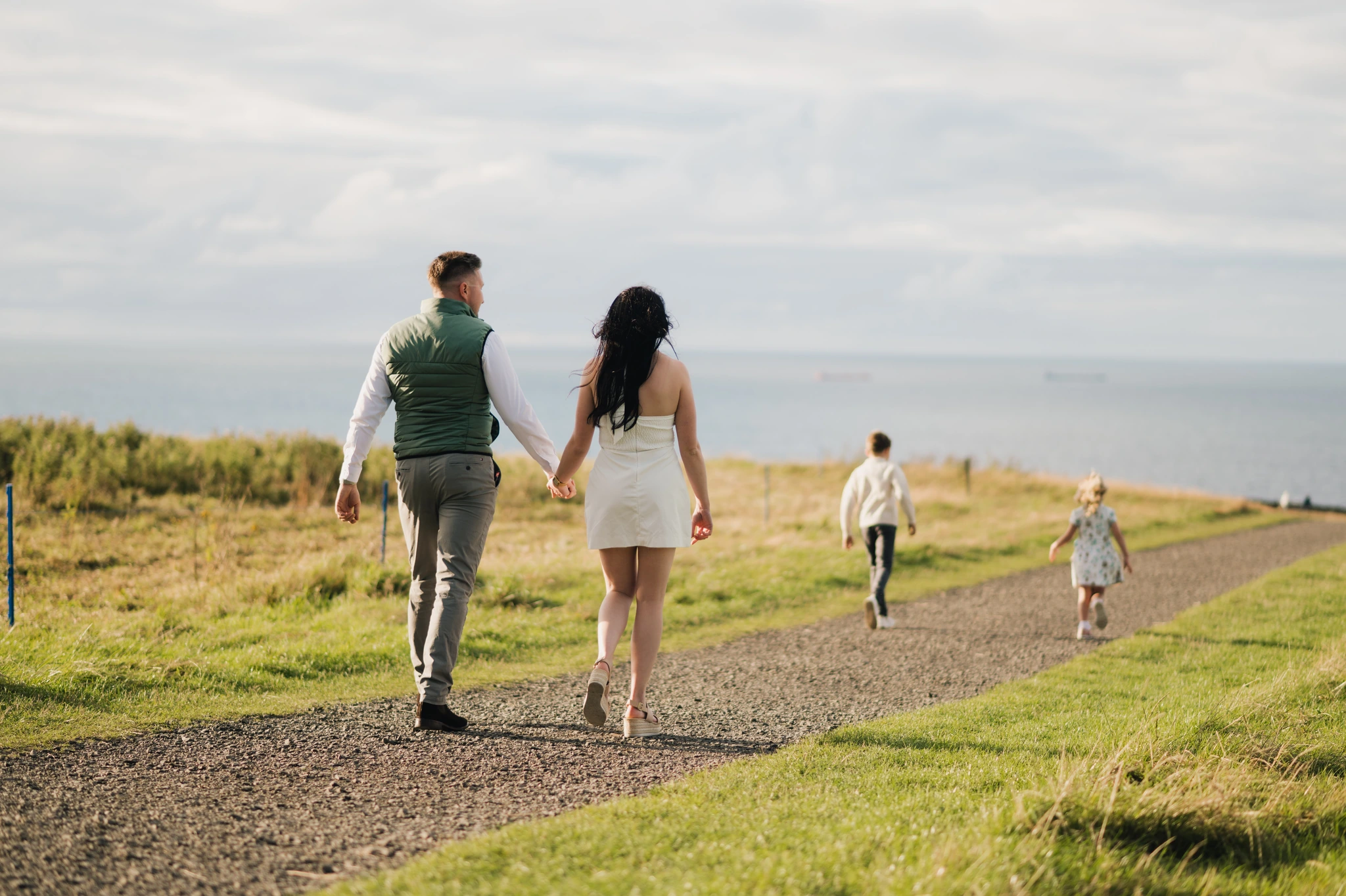 a bride and groom walk down a path towards the sea