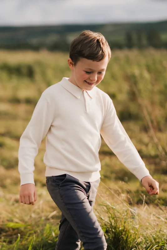 a boy wearing a white polo shirt in a grassy field