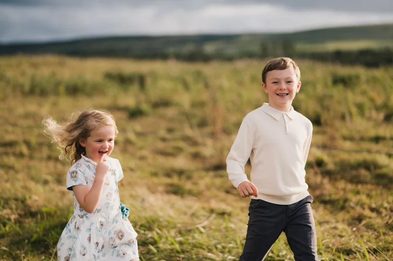 a boy and girl play in a grassy field with a cloudy sky