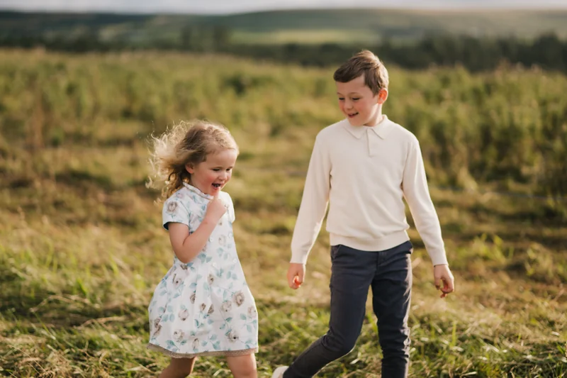 a boy and girl play in a grassy field